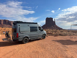Camper van (RV rental) and bikes parked at iconic Monument Valley for desert adventure.
