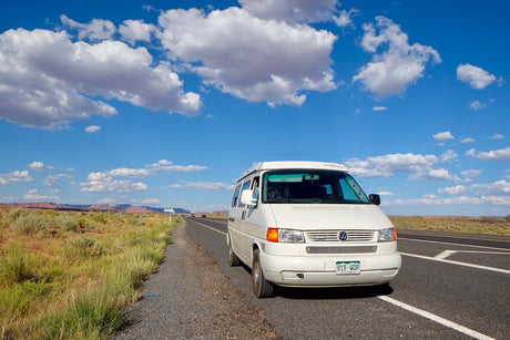 Enjoying the view from a white camper van RV rental on a desert road trip. Blue sky, clouds, and distant mountains.