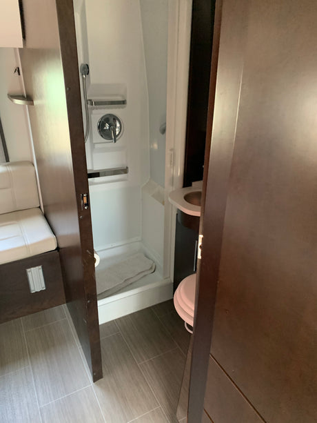 Inside an RV rental: compact bathroom with shower, toilet, and sink, seen from an open doorway next to bench seating.