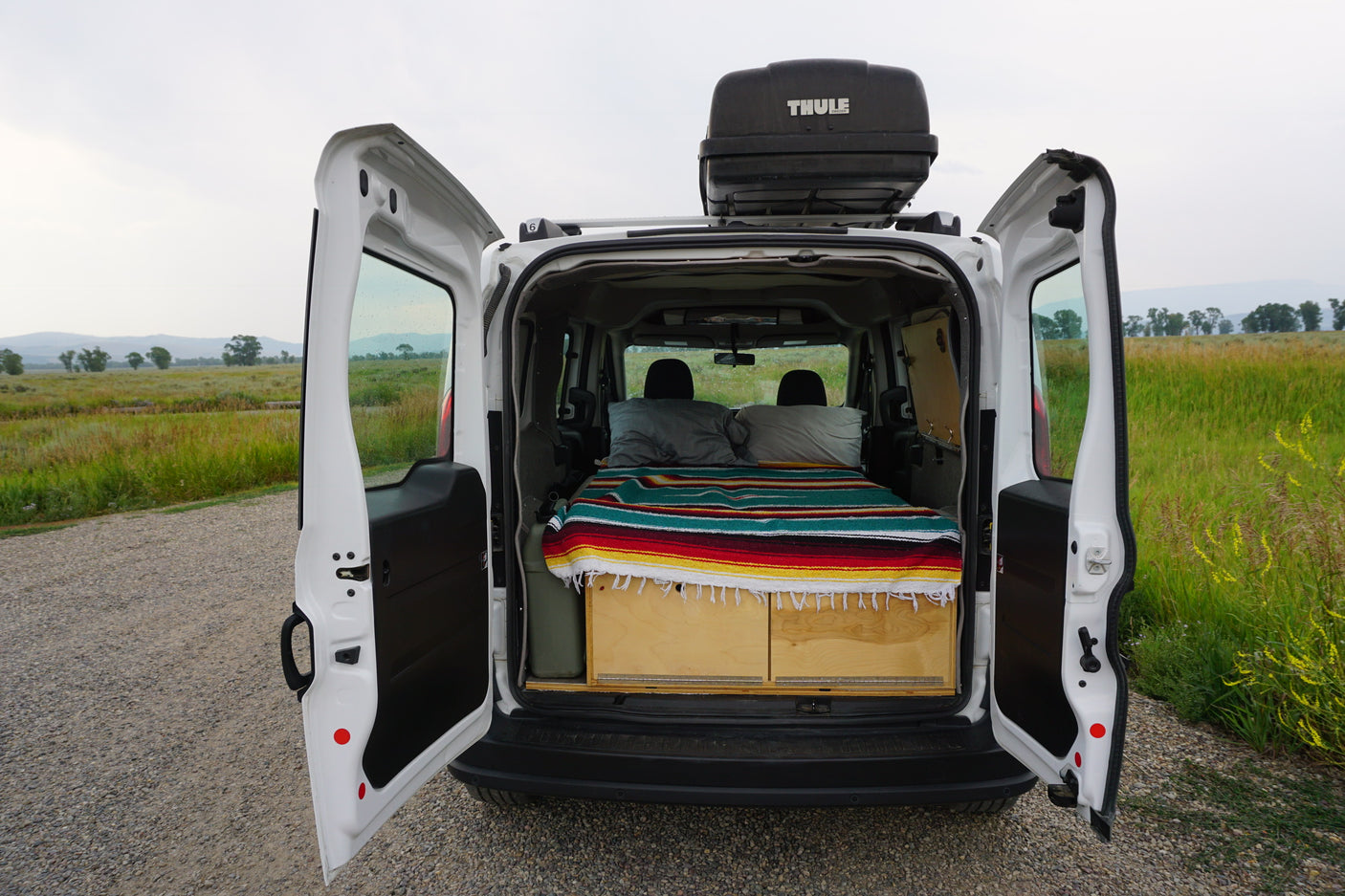 This camper van interior, ideal for an rv rental, features a bed, storage, and Thule roof box, ready for nature adventures.
