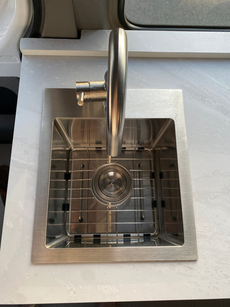 Stainless steel sink with grid, faucet, and bright countertop in an RV rental interior.