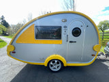 Side view of a compact, yellow and grey teardrop travel trailer, perfect for an RV rental or camping adventure.