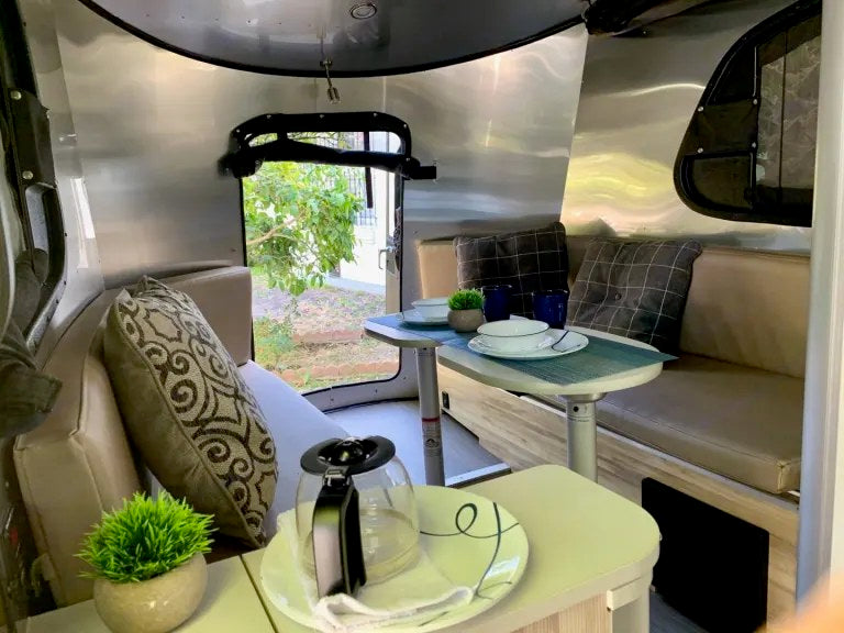 Inviting RV rental interior: shiny silver walls, dining table with place settings, plush seating, & coffee pot. — photo 6
