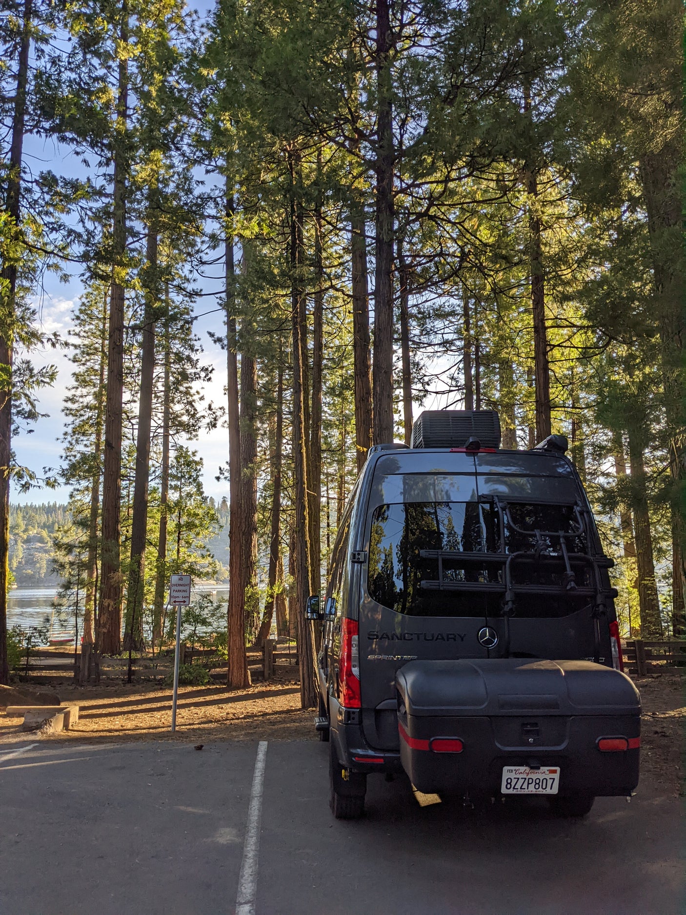 Enjoy nature with this RV rental camper van parked among tall trees by a serene lake. Ideal for outdoor escapes.