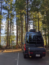 Enjoy nature with this RV rental camper van parked among tall trees by a serene lake. Ideal for outdoor escapes.