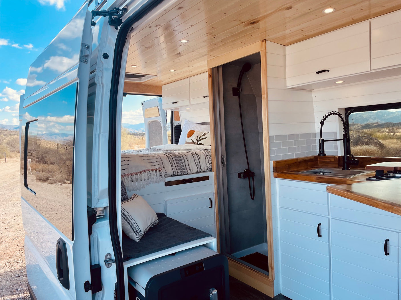 Stylish RV rental interior with a cozy bed, shower, and kitchenette. Enjoy van life with stunning desert views outside.