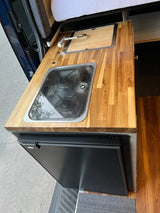 RV rental's compact kitchen: wooden countertop with sink, stove, and a built-in fridge.