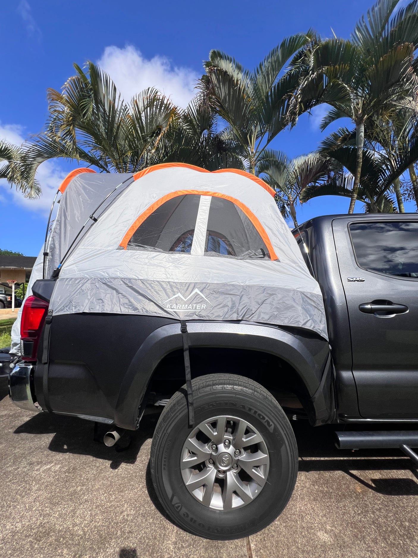 Dark grey truck with KARMATER truck bed tent under palm trees, an alternative to an RV rental for outdoor camping.