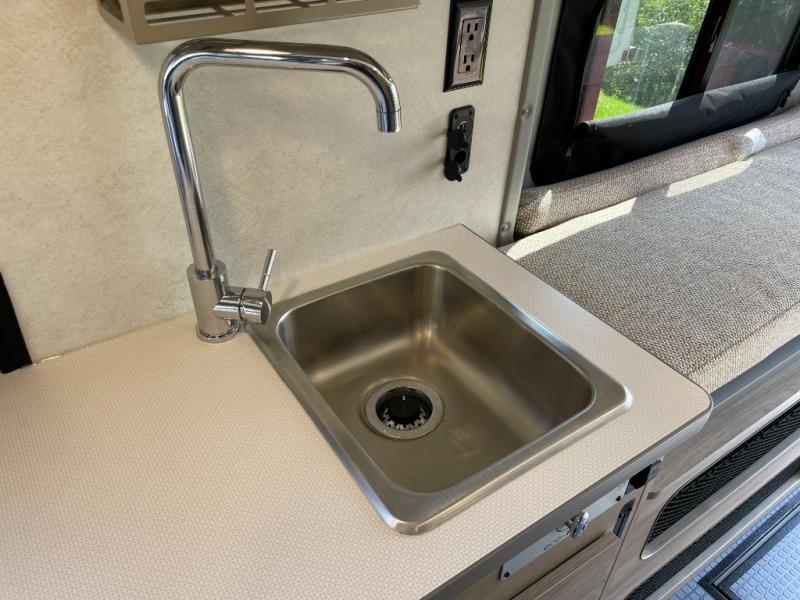 An RV rental interior showing a compact stainless steel sink, modern faucet, and versatile seating space.