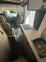 Inside an rv rental, featuring a compact kitchen with sink & cooktop, and front cockpit. Ideal for travel adventures.