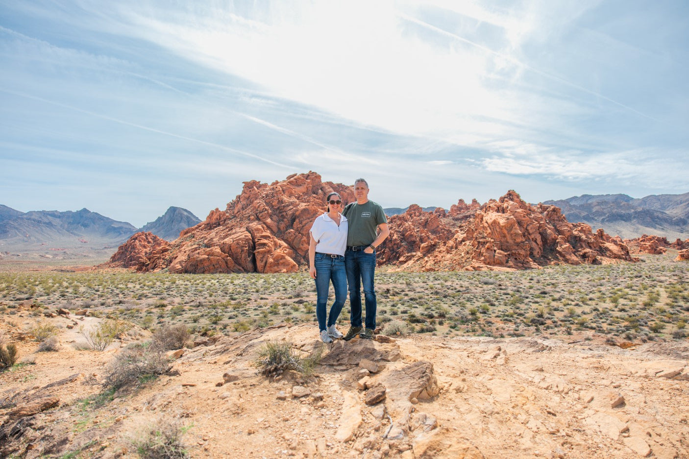 A couple explores a stunning red rock desert, an ideal setting for an RV rental getaway, under a blue sky with distant mountains.