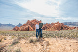 A couple explores a stunning red rock desert, an ideal setting for an RV rental getaway, under a blue sky with distant mountains.
