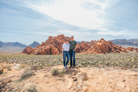 A couple explores a stunning red rock desert, an ideal setting for an RV rental getaway, under a blue sky with distant mountains.