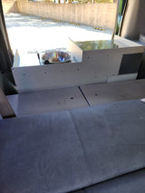 RV rental interior with a custom-built unit featuring a stainless steel sink and faucet, alongside gray fabric seating or a bed.