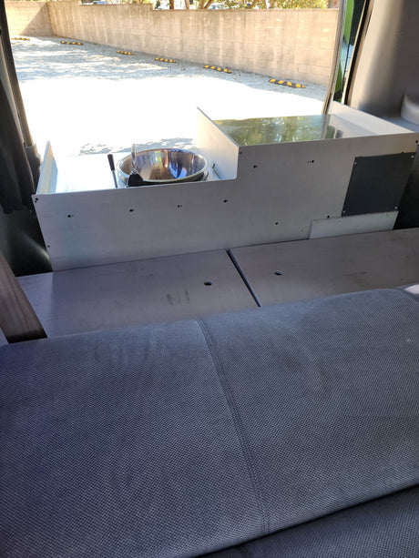 RV rental interior with a custom-built unit featuring a stainless steel sink and faucet, alongside gray fabric seating or a bed.