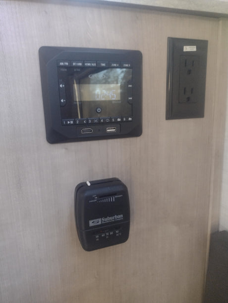 RV rental interior: Jensen media panel, Suburban thermostat, and power outlet on the wall, managing onboard systems.