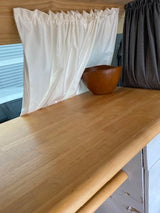 RV rental: Compact sleeping space with white ruffled bedding, a wooden bowl, and light wood built-ins.