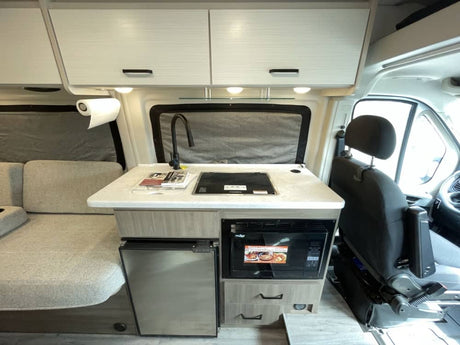 RV rental camper van interior features a compact kitchenette with sink, stove, microwave, fridge, and a comfortable sofa.