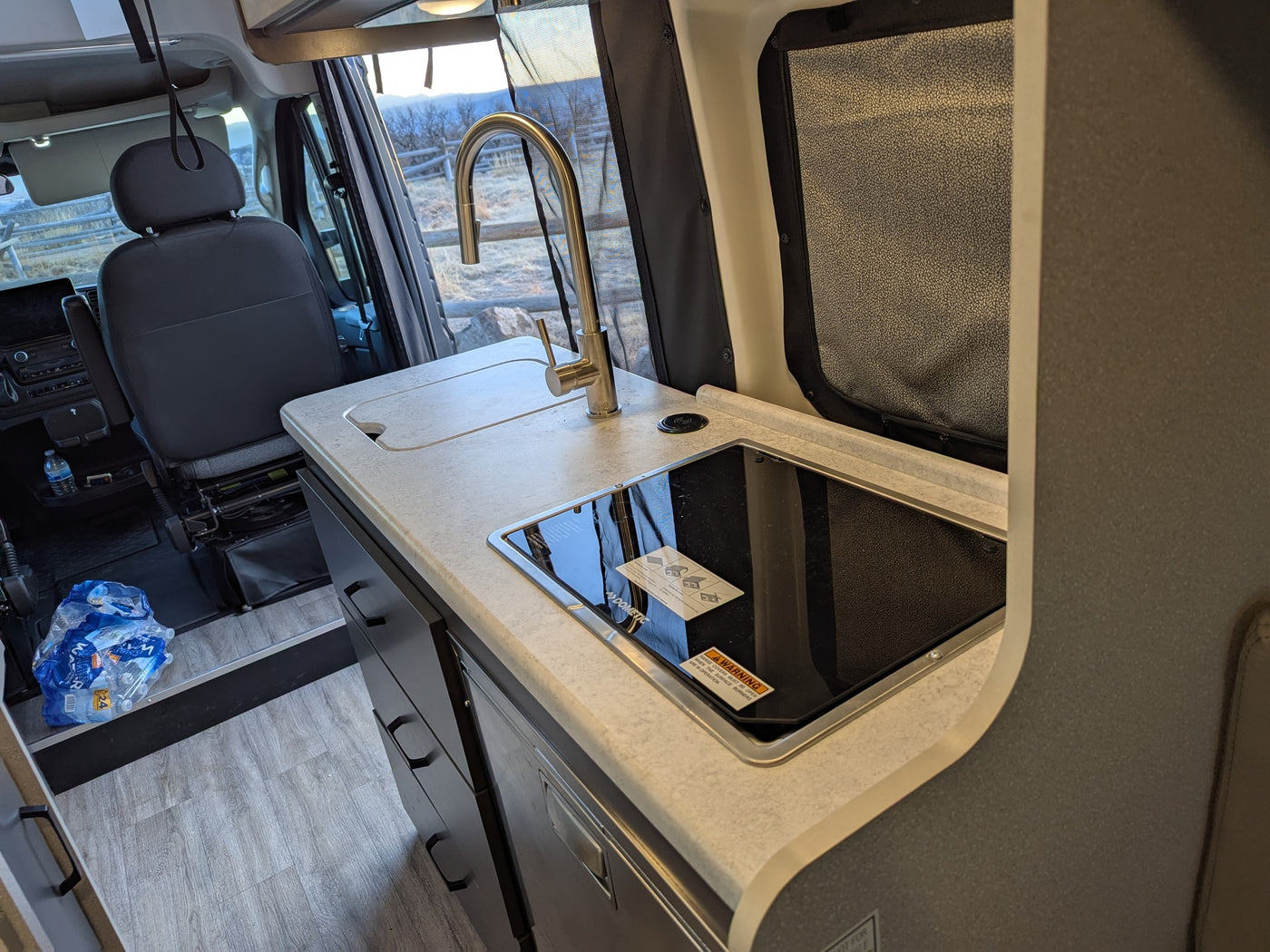 This RV rental interior showcases a functional kitchen counter with sink, faucet, and a Dometic cooktop, ready for your road trip. — photo 8