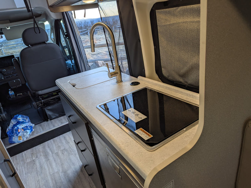 This RV rental interior showcases a functional kitchen counter with sink, faucet, and a Dometic cooktop, ready for your road trip. — photo 8