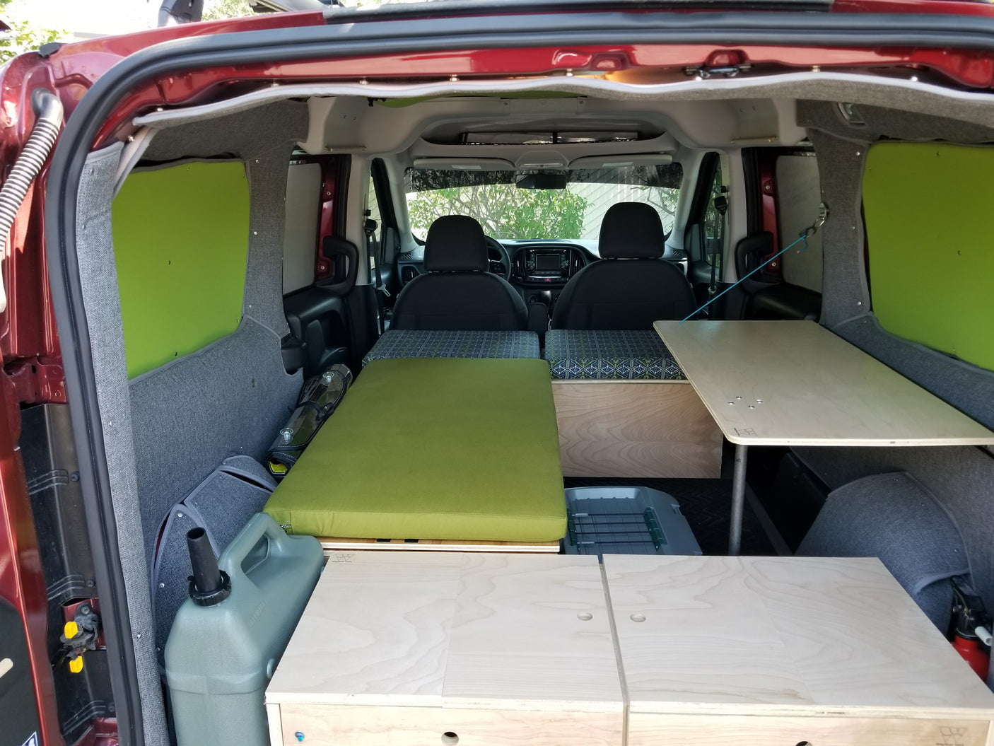 Interior of a custom camper van, highlighting a green cushion bed, wooden table, and storage for an RV rental getaway.