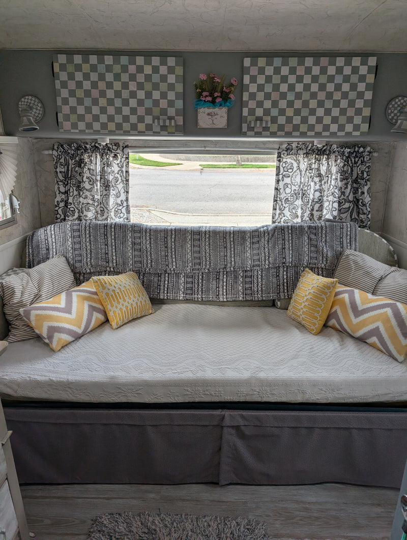 Cozy RV rental interior: daybed with yellow & striped pillows, patterned blanket, checkered decor, and roadside window view. — photo 3