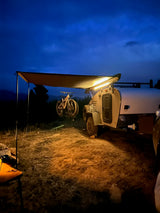 Night camping with an RV rental: Illuminated teardrop trailer, awning, and mountain bikes set up under a dark blue sky.