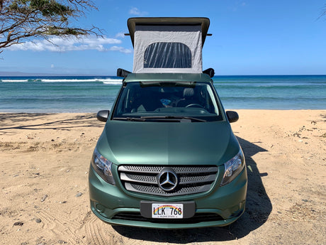 Green Mercedes-Benz RV rental with pop-top extended, parked on a sunny Hawaii beach beside the ocean.