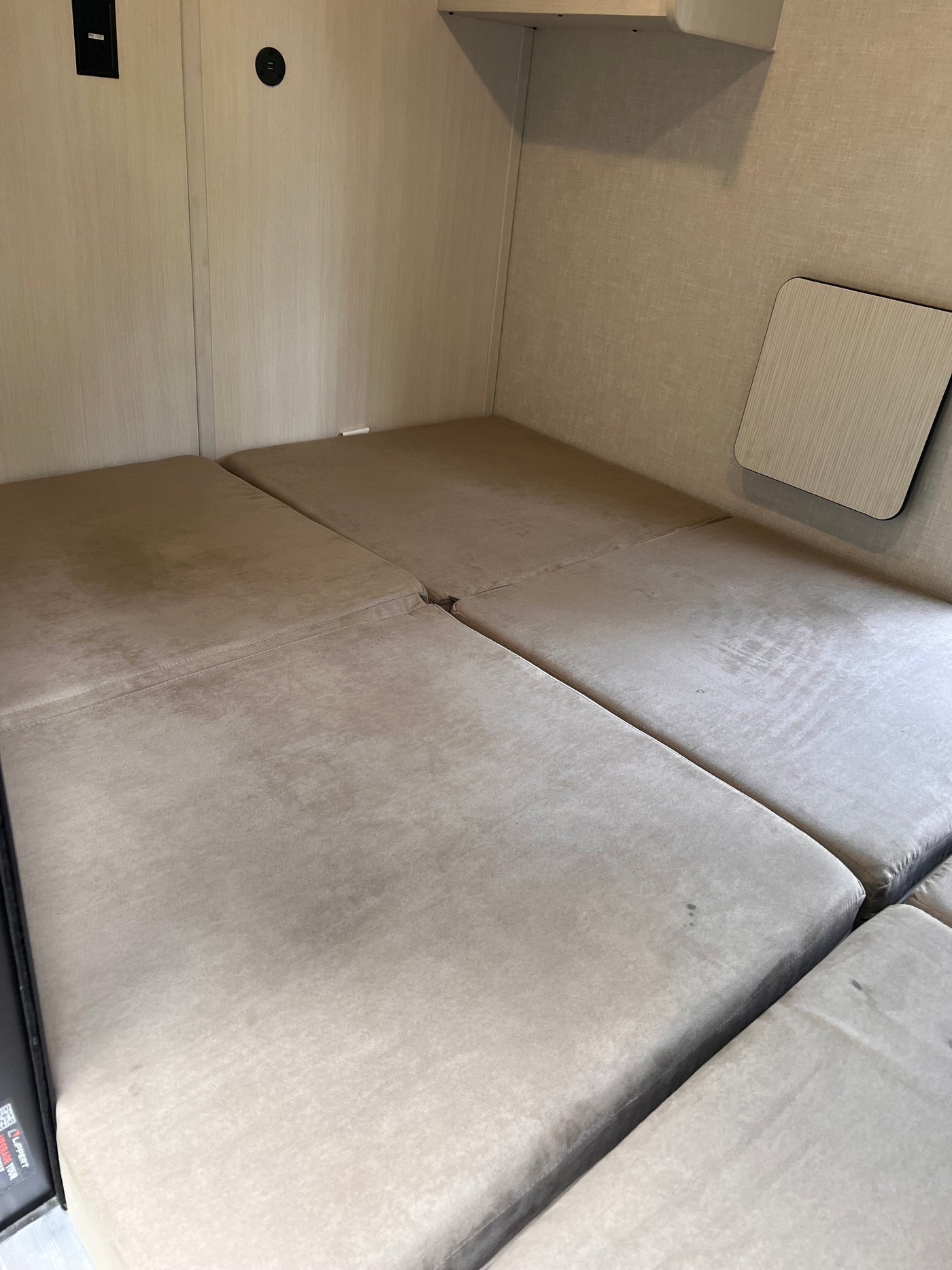 RV rental bed area with light-colored upholstered cushions, wall paneling, and charging ports. A small table is on the right. — photo 9