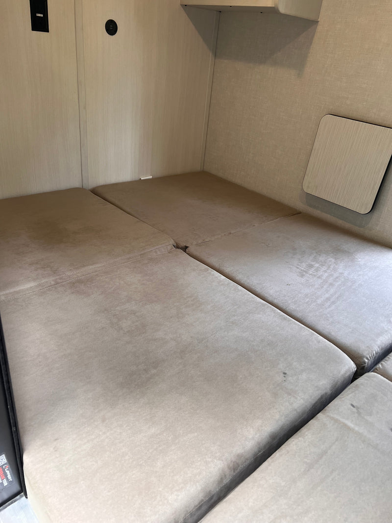 RV rental bed area with light-colored upholstered cushions, wall paneling, and charging ports. A small table is on the right. — photo 9