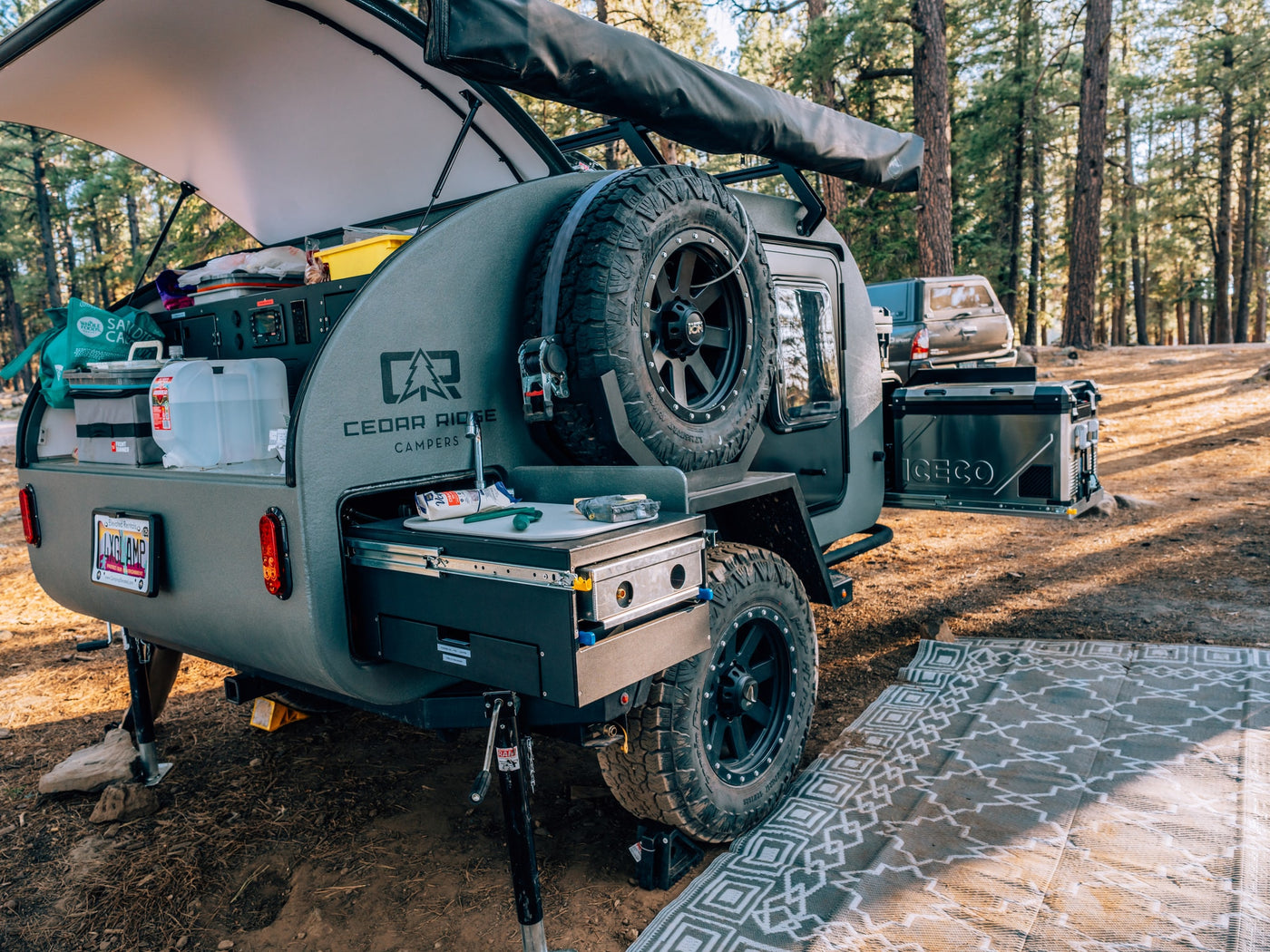 Cedar Ridge RV rental teardrop camper with an outdoor kitchen, spare tire, and ICECO fridge ready for forest camping. — photo 7