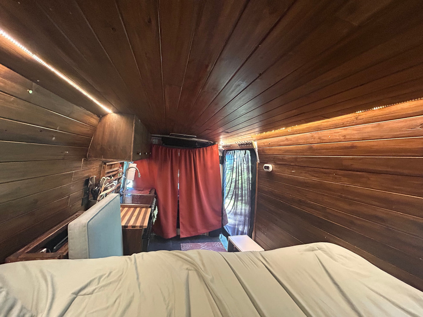 RV rental: Cozy wooden interior featuring a comfortable bed, a compact kitchen area with a sink, and privacy curtains. — photo 19