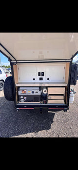 This rv rental features a compact outdoor kitchen in a trailer, with a Dometic fridge, stainless counter, and storage drawers.