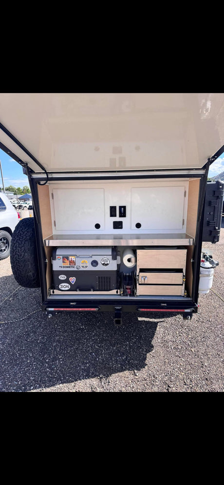 This rv rental features a compact outdoor kitchen in a trailer, with a Dometic fridge, stainless counter, and storage drawers.