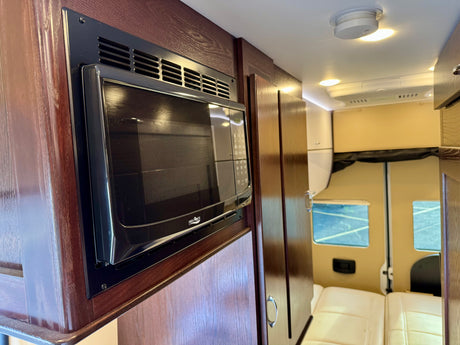 RV rental interior: Built-in microwave oven, dark wood cabinetry, and cream seating area visible inside the vehicle.