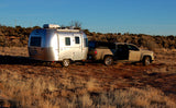 Explore the outdoors with an RV rental: An Airstream trailer hitched to a pickup truck in a scenic, arid landscape.