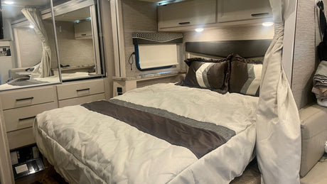 Cozy RV rental bedroom with modern decor, a comfortable bed, mirrored storage, and overhead cabinets.