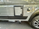 Side of an RV rental, showing a utility access panel, electrical inlet, and gray water tank drain valve for waste disposal.