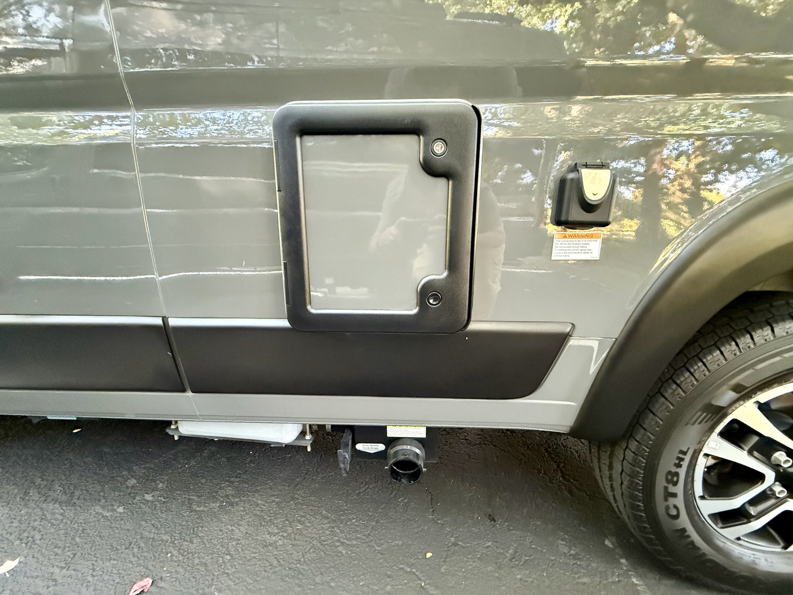 Side of an RV rental, showing a utility access panel, electrical inlet, and gray water tank drain valve for waste disposal.