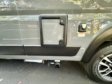 Side of an RV rental, showing a utility access panel, electrical inlet, and gray water tank drain valve for waste disposal.