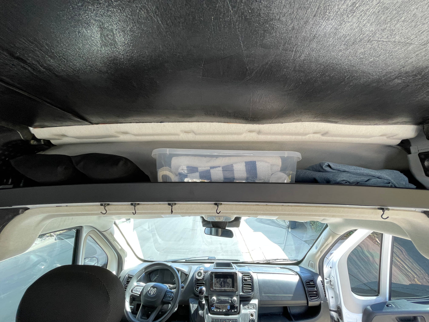 RV rental interior view: overhead storage with bin and blankets, and the vehicle's front dashboard and steering wheel.