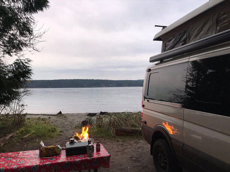 Enjoying an rv rental van by the serene waterfront. Cozy campfire and outdoor cooking make for perfect camping.