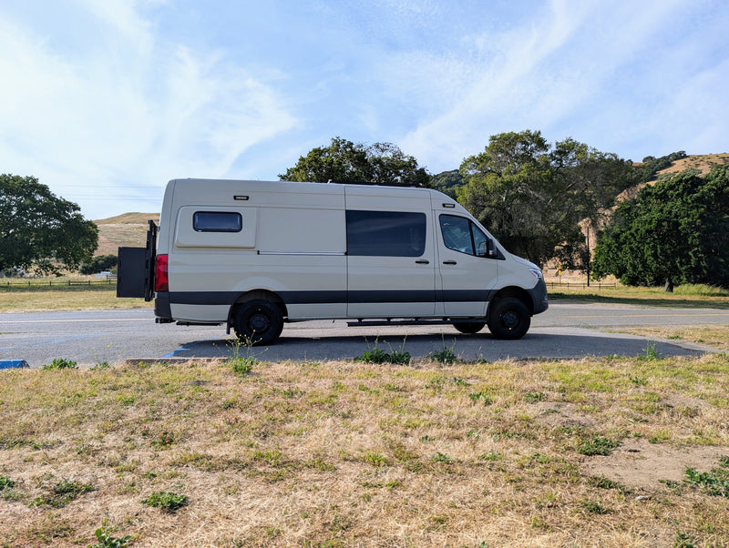 Beige RV rental camper van parked on an asphalt lot, with dry grass and rolling hills in the background. — photo 9