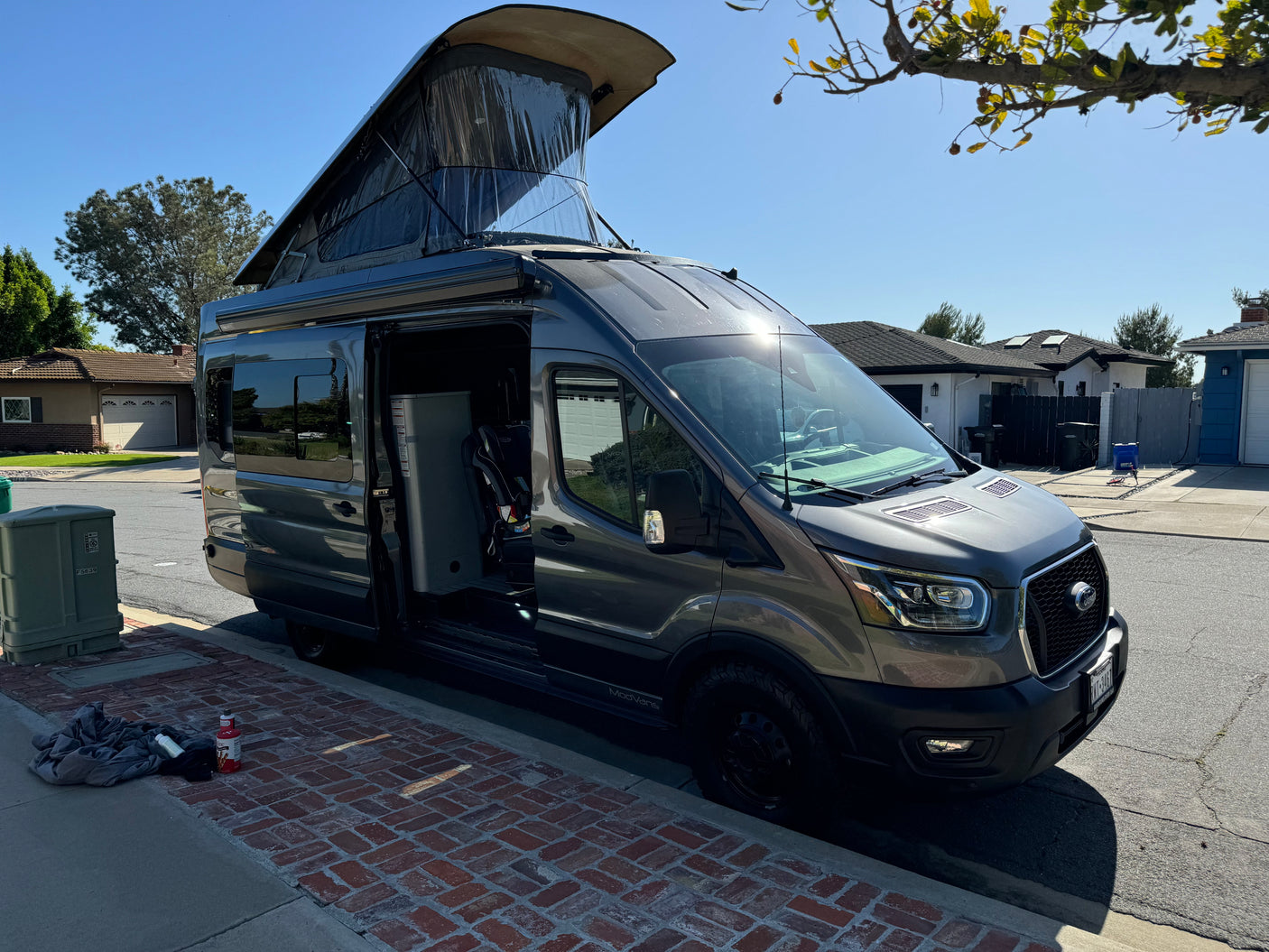 Grey camper van, ideal for an RV rental, parked on a sunny street with its pop-top roof raised and driver's door open.