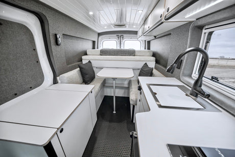 Explore a sleek rv rental camper van interior. White counters, gray walls, bed, kitchen, and dining for your adventures.
