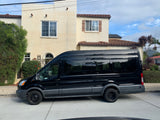 A black Ford Transit van, ideal for RV rental, parked on a paved drive in front of a stucco house with a tiled roof.