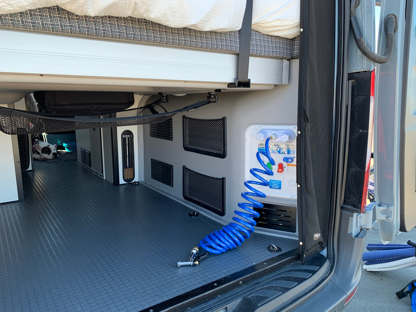 RV rental interior: organized storage, water station with blue hose, durable flooring, and a cozy spot for a dog.