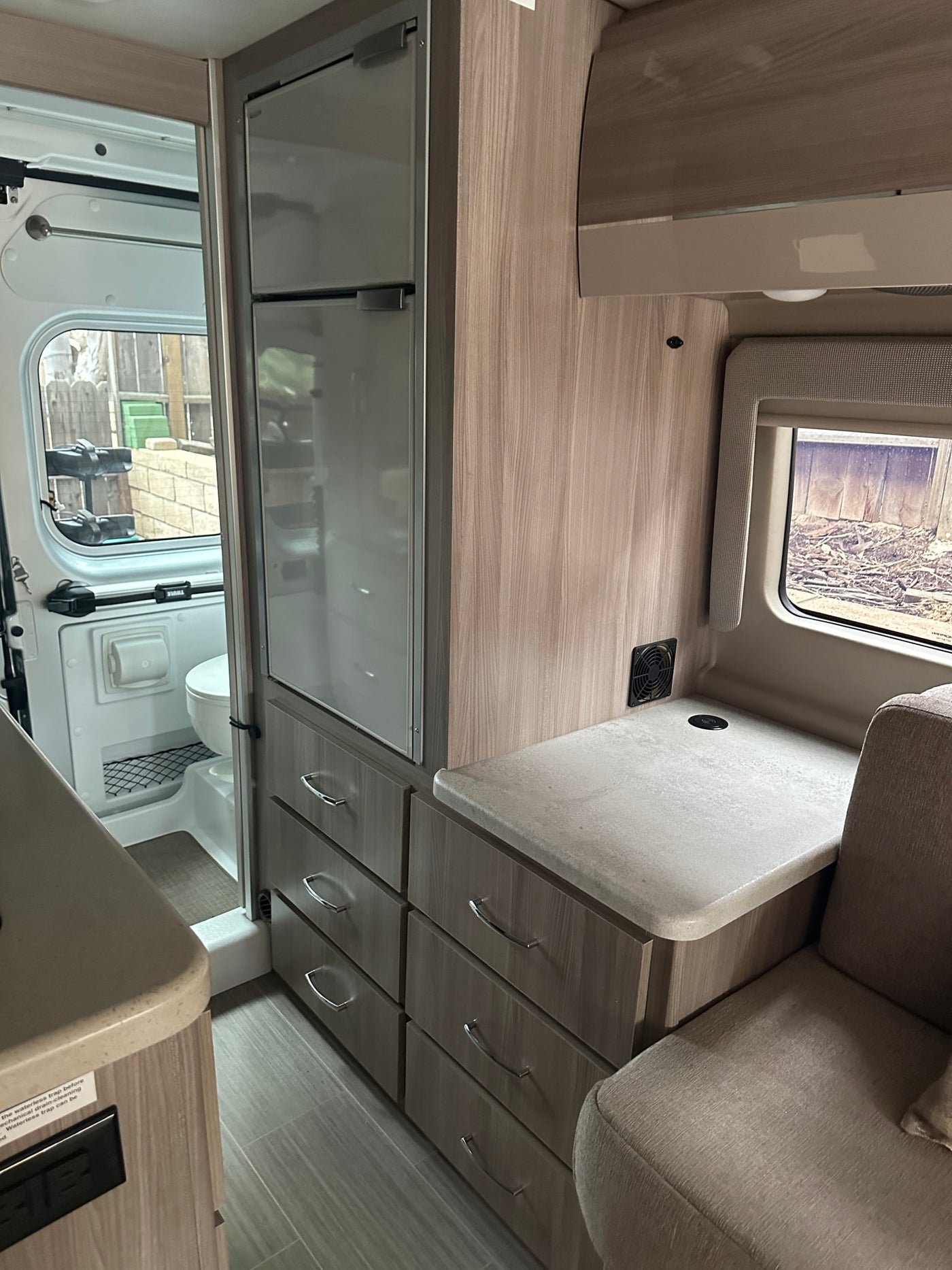 Inside an RV rental: modern compact interior with a refrigerator, multiple drawers, countertop, and a peek into the wet bath. — photo 4