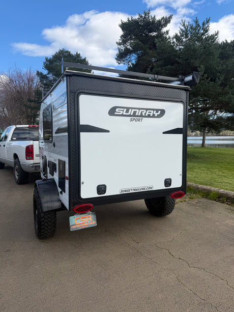 Sunray Sport RV rental trailer with aggressive off-road tires, parked lakeside, ready for adventure.
