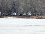 RVs and vehicles parked for winter camping by a frozen lake, surrounded by bare trees. An ideal rv rental adventure.